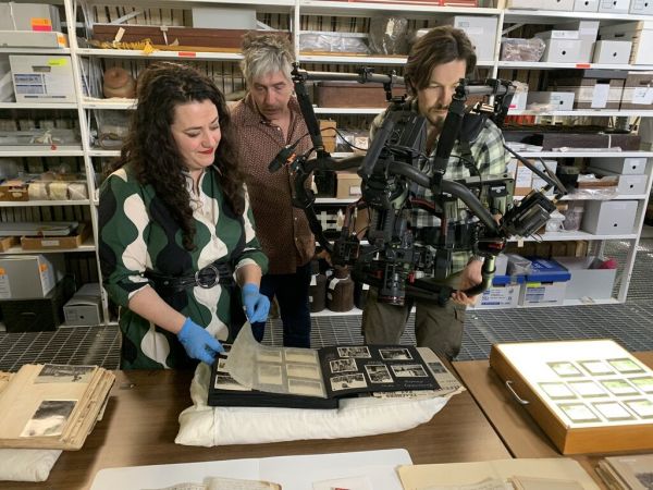 Three people stand in the archives, filming a document.